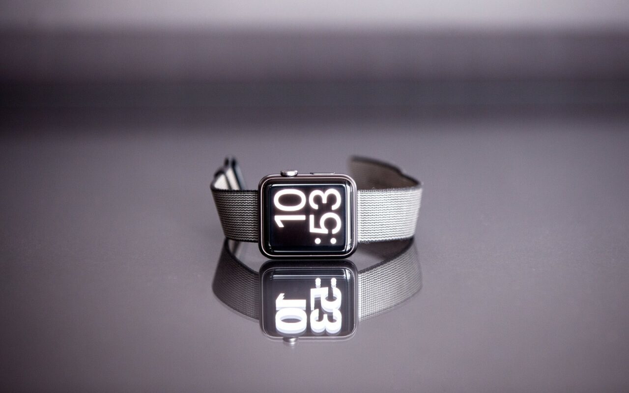 Une montre connectée posée sur la tranche, bracelet déployé, sur fond clair.