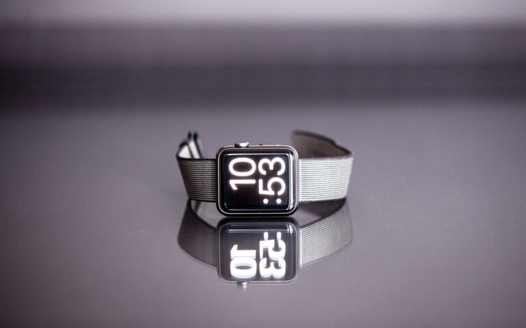 Une montre connectée posée sur la tranche, bracelet déployé, sur fond clair.
