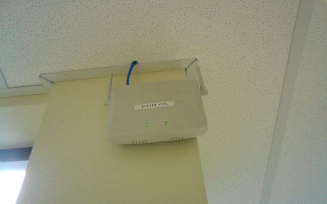 Une borne Wi-Fi blanche fixée sous un plafond, reliée par un câble réseau bleu