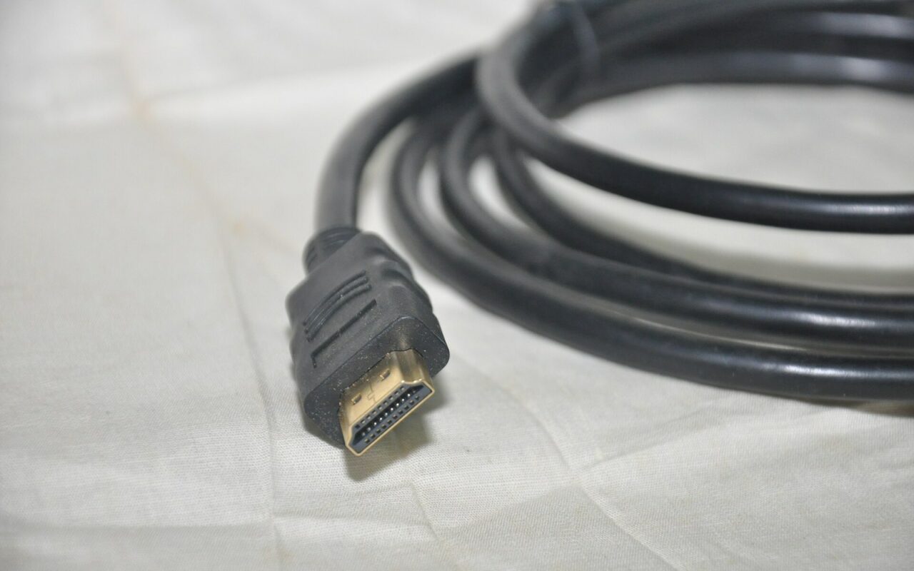 Câble HDMI noir enroulé, connecteur type A aux contacts dorés, posé sur un tissu clair
