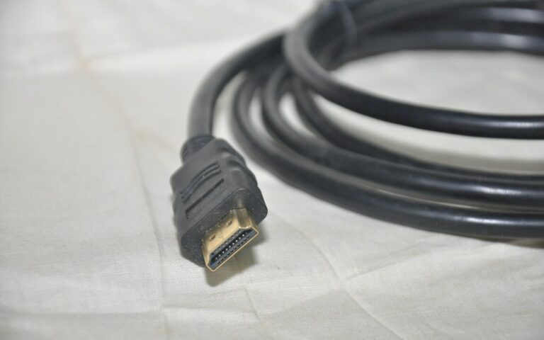 Câble HDMI noir enroulé, connecteur type A aux contacts dorés, posé sur un tissu clair