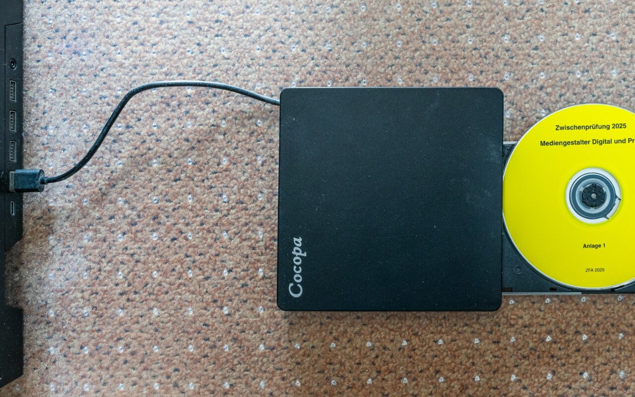 Un lecteur de disque optique externe relié par un câble, à côté d’un disque compact.