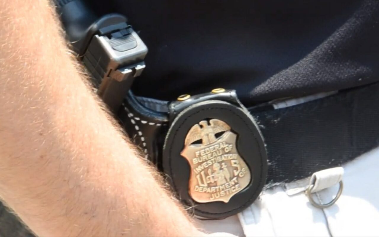 Insigne doré du FBI accroché à la ceinture d'un agent, à cÎté de son arme