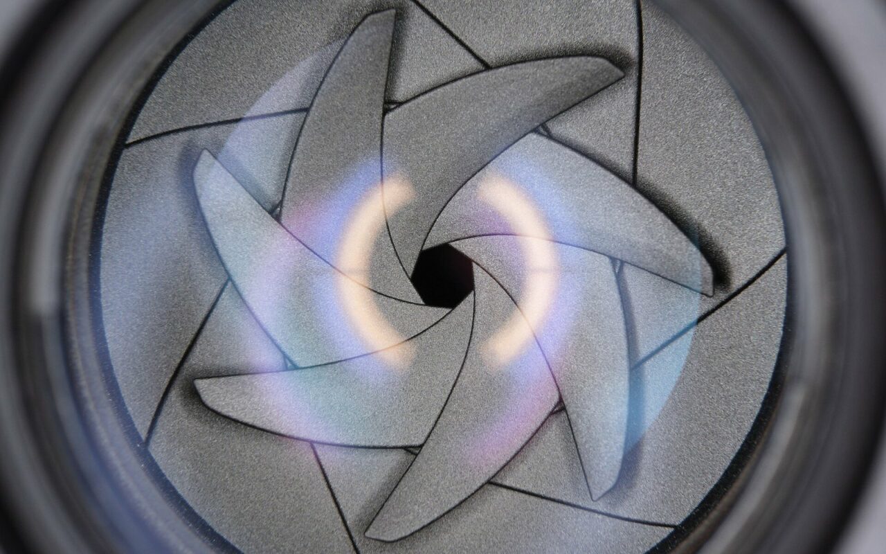 Gros plan sur les lamelles d’un diaphragme d’objectif photo, refermées en étoile autour d’une petite ouverture centrale