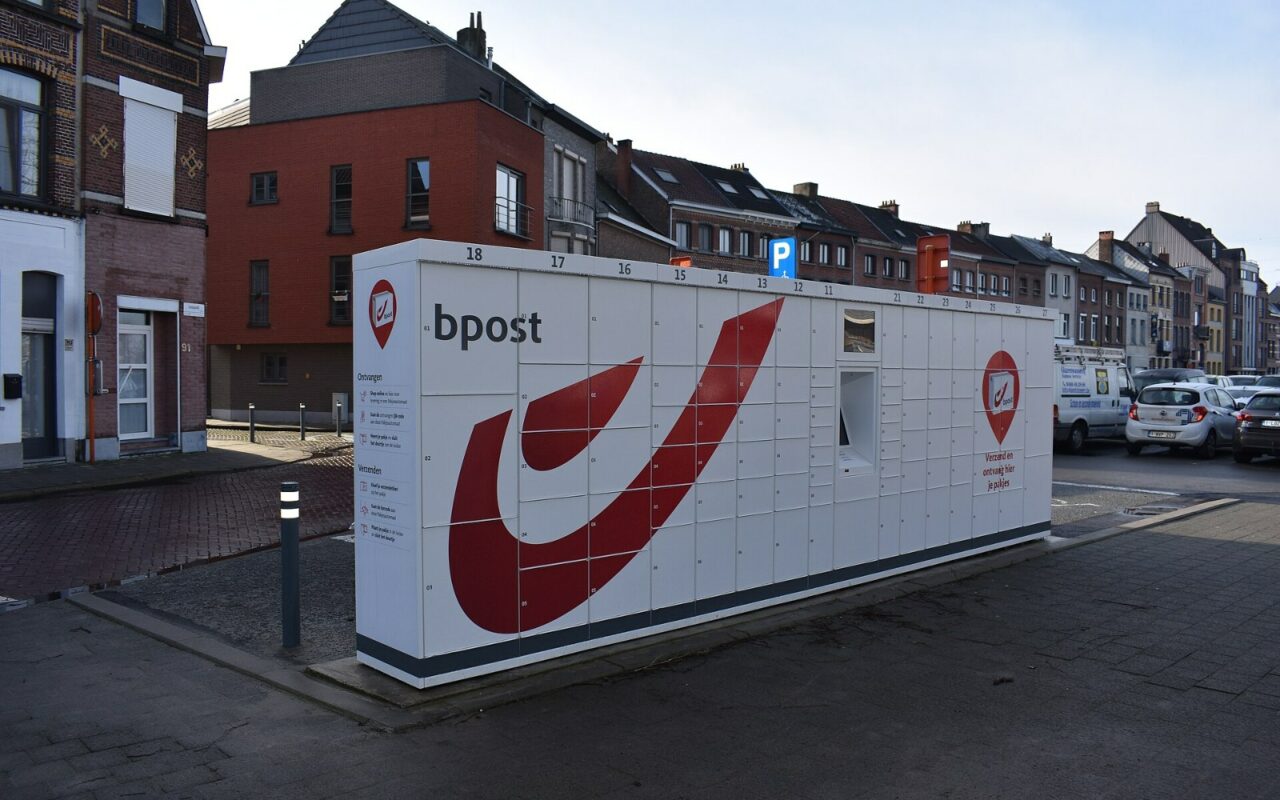 Automate à colis bpost blanc et rouge installé sur une place, avec ses casiers fermés