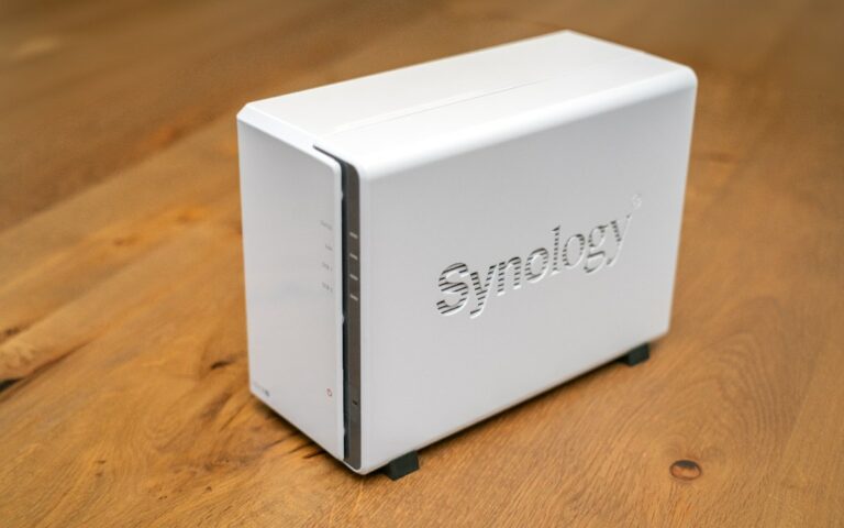 Petit boîtier NAS Synology blanc à 2 baies, posé sur un plateau en bois clair