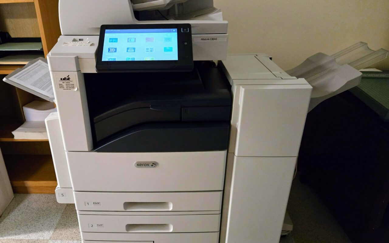 Un grand copieur multifonction de bureau, capot fermé, dans un couloir.