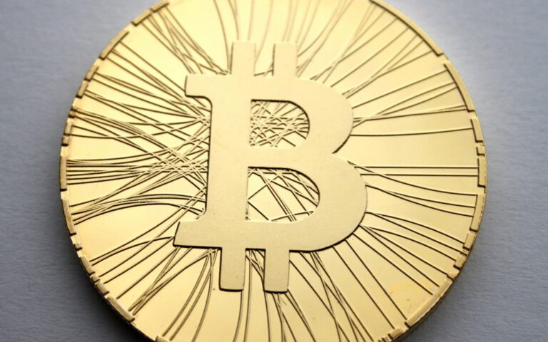 Piece metallique portant le symbole du bitcoin, posee sur une surface sombre