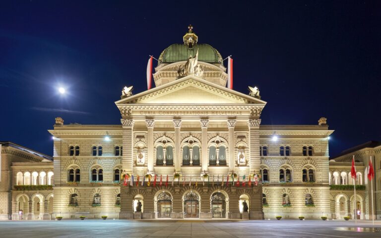 Facade du palais federal suisse eclairee de nuit, drapeaux sur la place