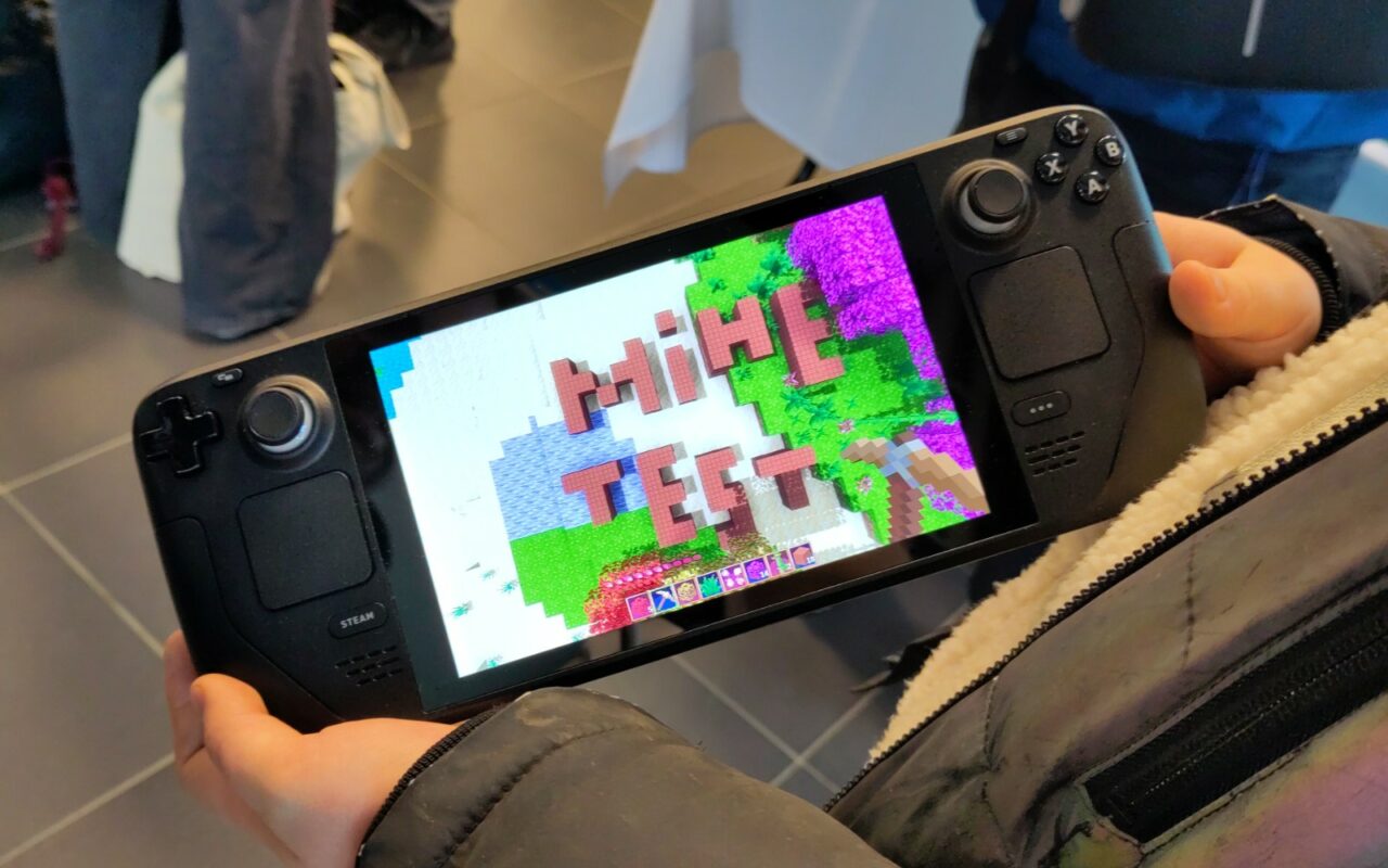 Console portable Steam Deck tenue à deux mains, affichant un jeu en pixel art