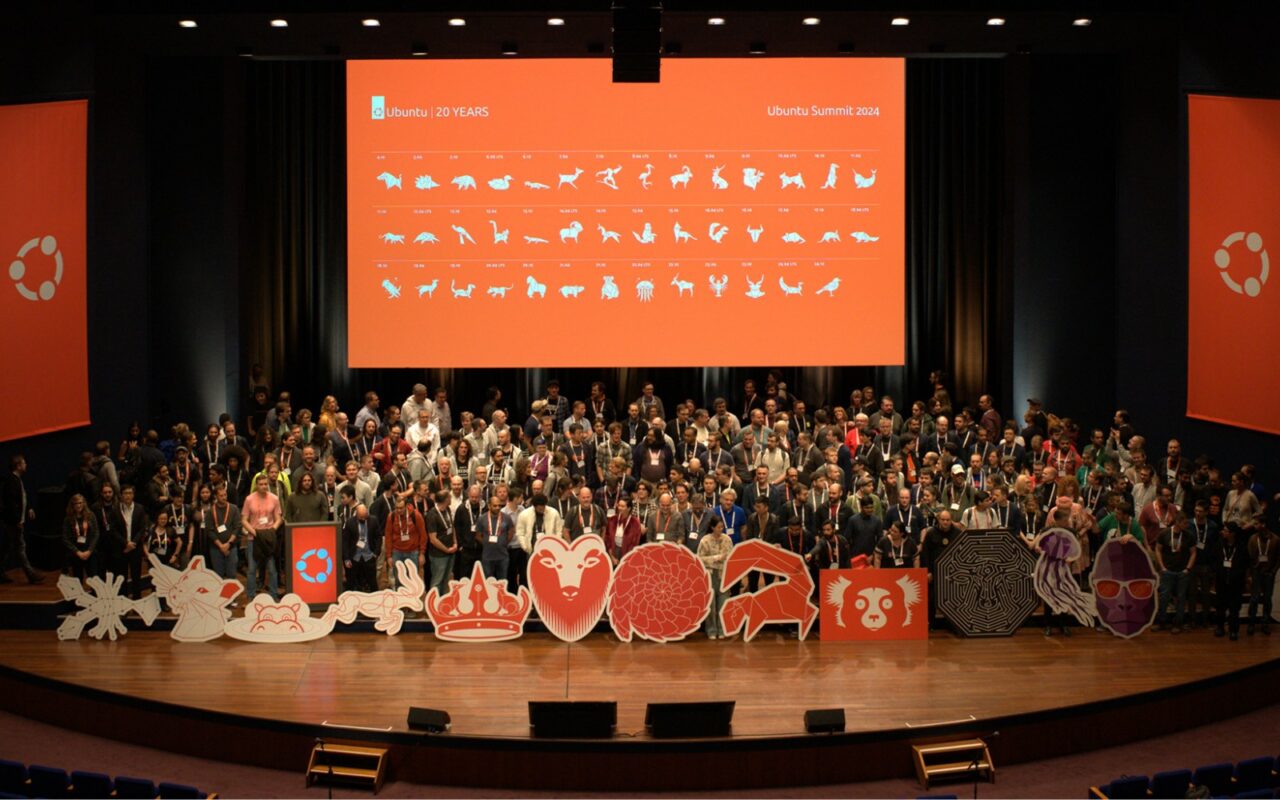 Des centaines de participants rassemblés sur la scène du Ubuntu Summit devant un écran orange aux couleurs d'Ubuntu