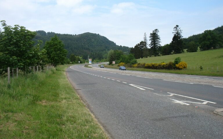 Route A9 à deux voies bordée d'herbe et d'arbres, collines boisées en arrière-plan, au nord de Pitlochry en Écosse