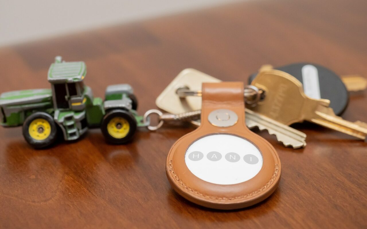 Trousseau de clés posé sur une table en bois, avec un AirTag dans un étui en cuir et une petite figurine de tracteur