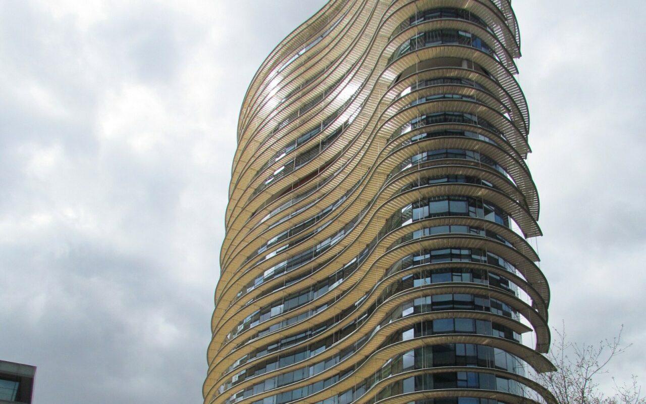 Une tour ronde aux étages soulignés de bandeaux clairs, vue en contre-plongée sous un ciel nuageux : le bâtiment informatique du fisc néerlandais à Apeldoorn.