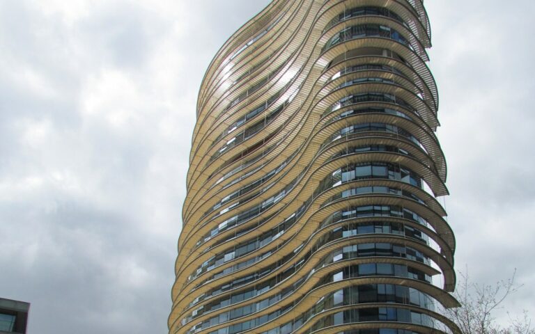 Une tour ronde aux étages soulignés de bandeaux clairs, vue en contre-plongée sous un ciel nuageux : le bâtiment informatique du fisc néerlandais à Apeldoorn.