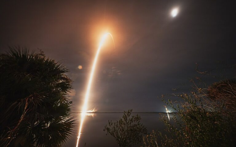 Trajectoire lumineuse d'une fusée Falcon 9 dans le ciel nocturne au-dessus de palmiers, lors du lancement de satellites BlueBird