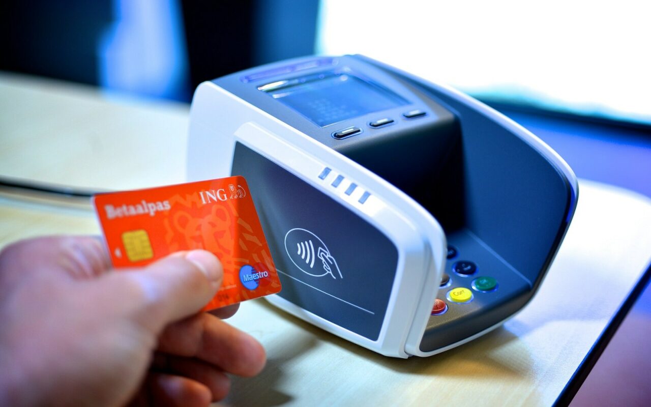 Une main présente une carte de débit orange à puce devant un terminal de paiement