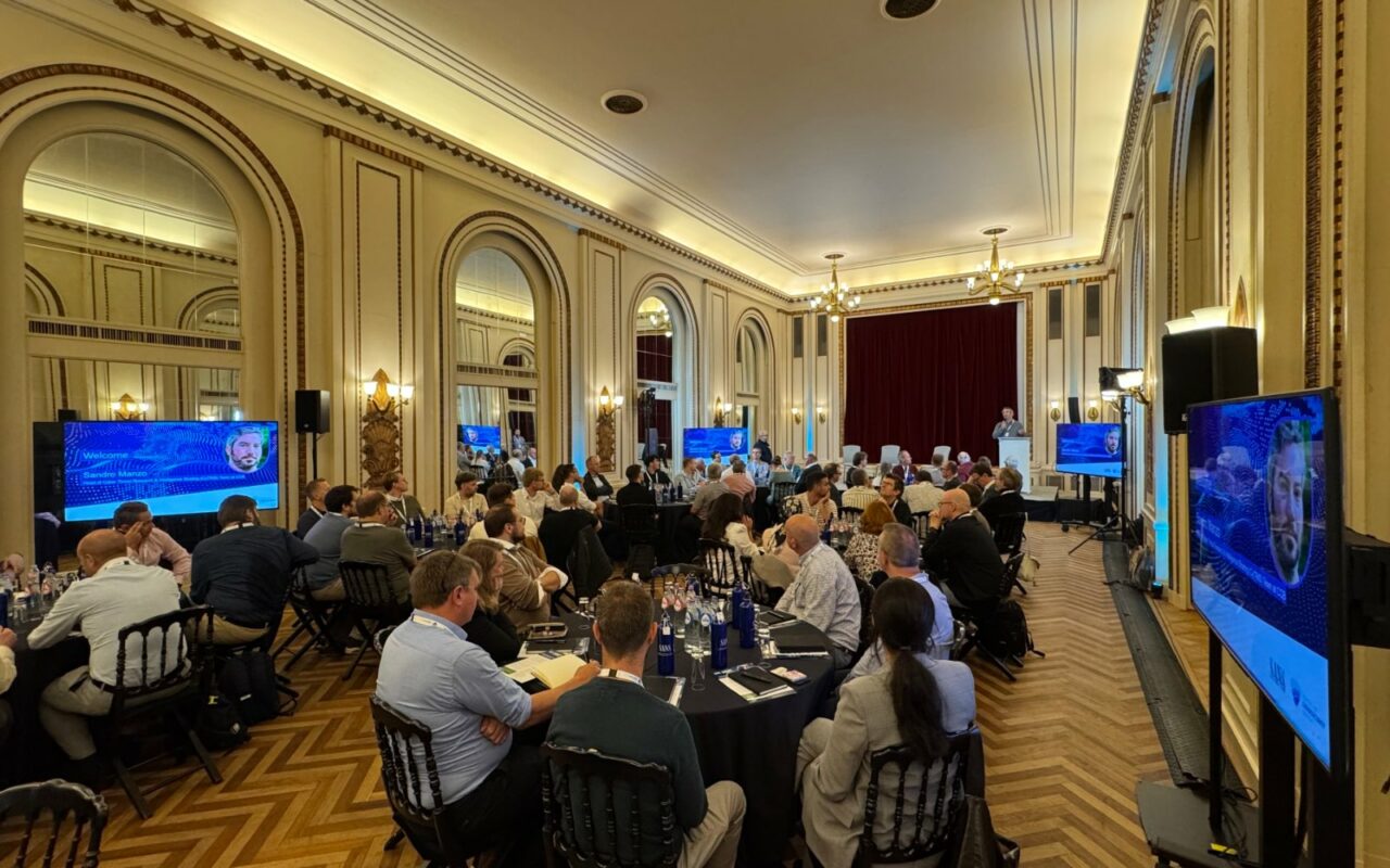 Salle de réception aux murs dorés remplie de participants assis à des tables rondes, face à plusieurs écrans, lors d'un exercice de crise cyber à Bruxelles