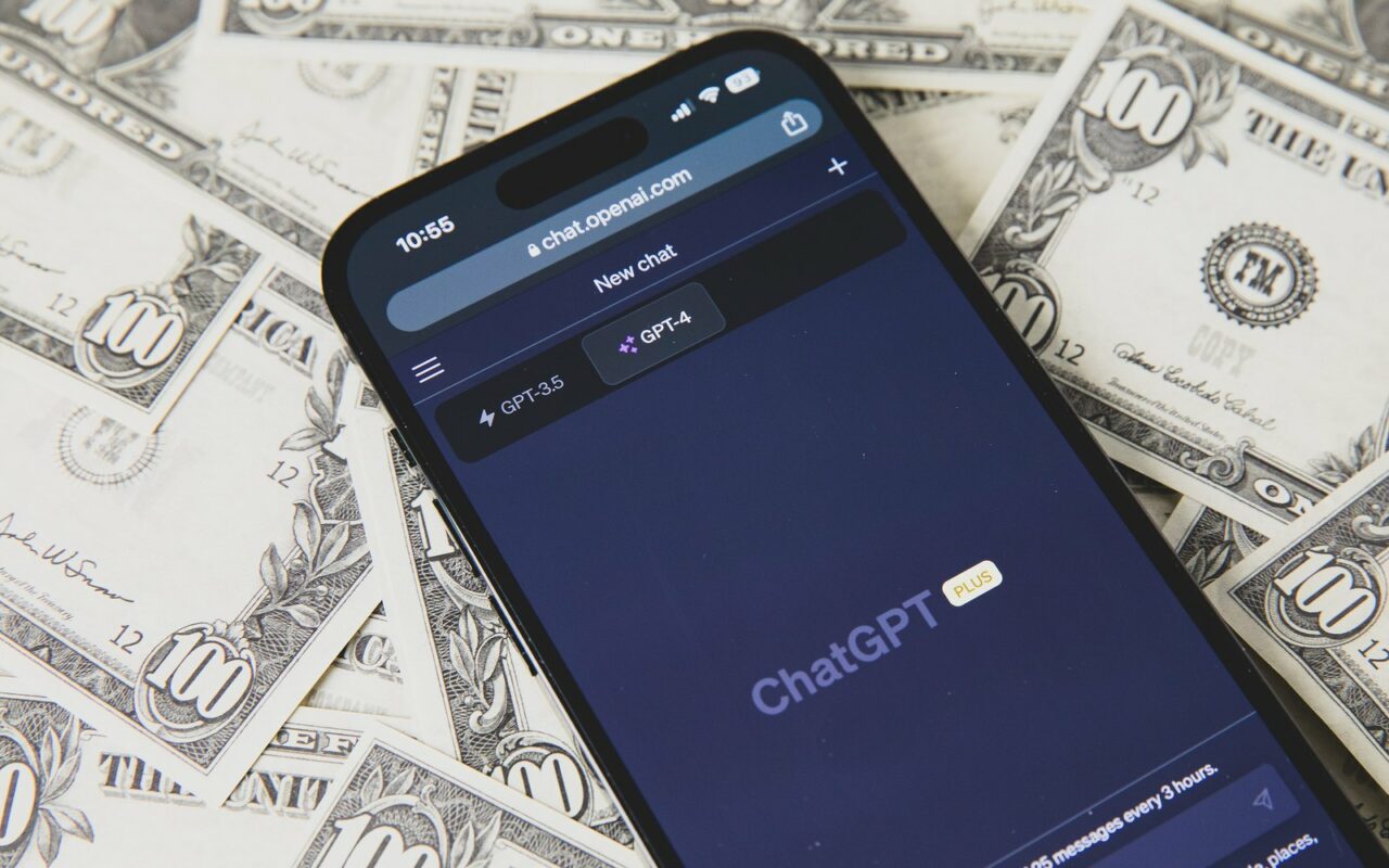 Smartphone affichant l'application ChatGPT posé sur des billets de 100 dollars