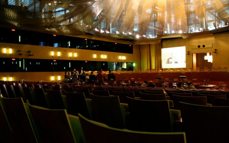 Grande salle d'audience de la Cour de justice de l'Union européenne à Luxembourg : rangées de sièges, écran au fond et plafond tendu de voilages dorés