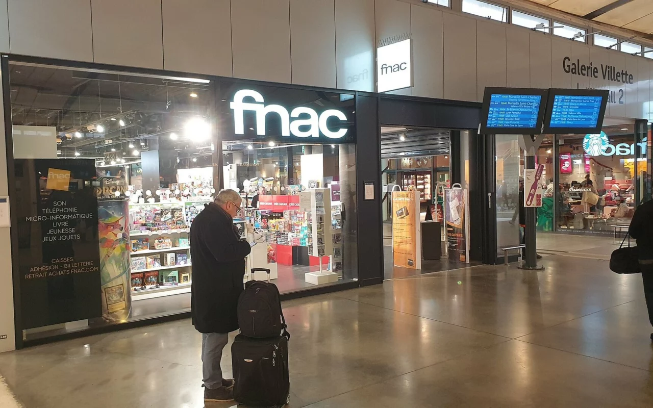 Entrée d'un magasin Fnac dans une galerie de gare, enseigne lumineuse, voyageur avec une valise devant la vitrine