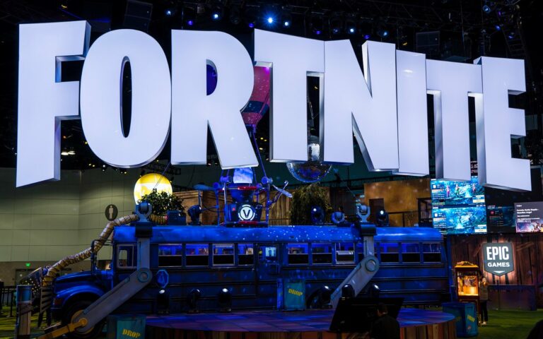 Immenses lettres lumineuses FORTNITE au-dessus du bus de combat bleu du jeu, sur le stand d'Epic Games dans un salon plongé dans la pénombre.
