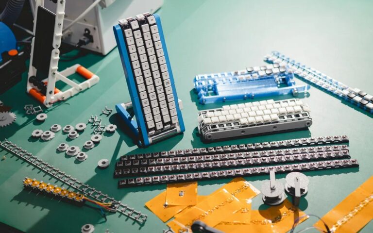 Pièces du clavier à tapis roulant de Google Japon étalées sur un tapis de découpe vert : touches, rouleaux, chaînes et circuits