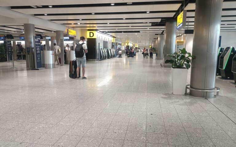 Hall des départs du terminal 3 de Heathrow, avec piliers, panneaux et quelques voyageurs
