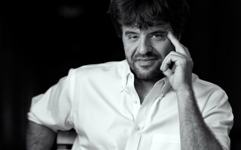 Portrait en noir et blanc de Karl Deisseroth, en chemise blanche, un doigt posé sur la tempe