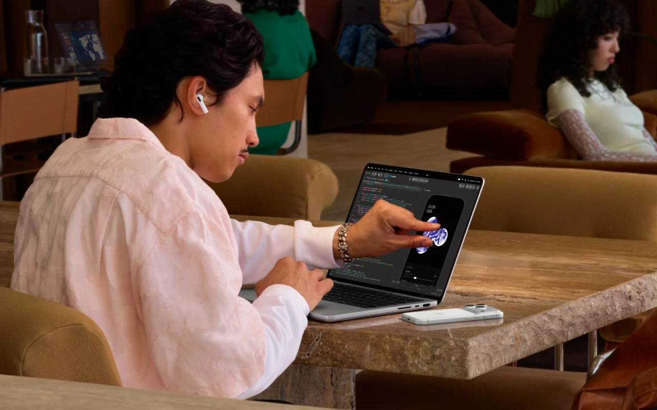 Un homme assis à une table touche du doigt l'écran d'un MacBook Pro pour manipuler un objet en 3D