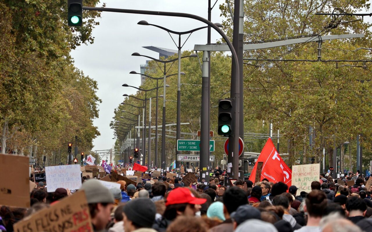 Foule de manifestants sur un large boulevard parisien bordé d'arbres, pancartes et drapeaux rouges levés