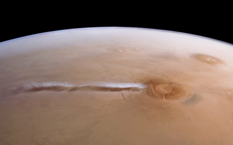 Vue orbitale de Mars : une longue traînée nuageuse blanche s'étire vers l'ouest depuis le volcan Arsia Mons