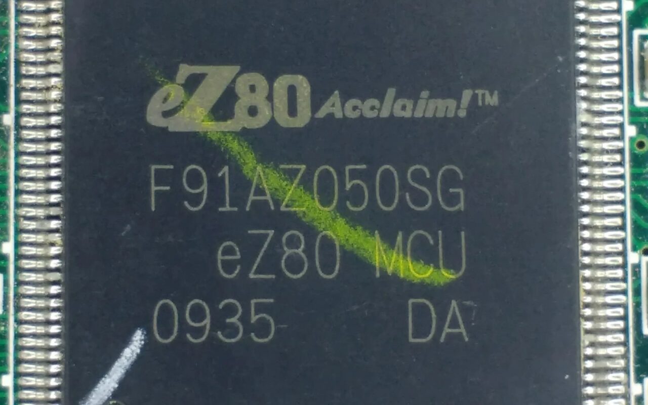 Gros plan sur une puce carrée marquée eZ80 Acclaim, référence F91AZ050SG, soudée sur un circuit imprimé.