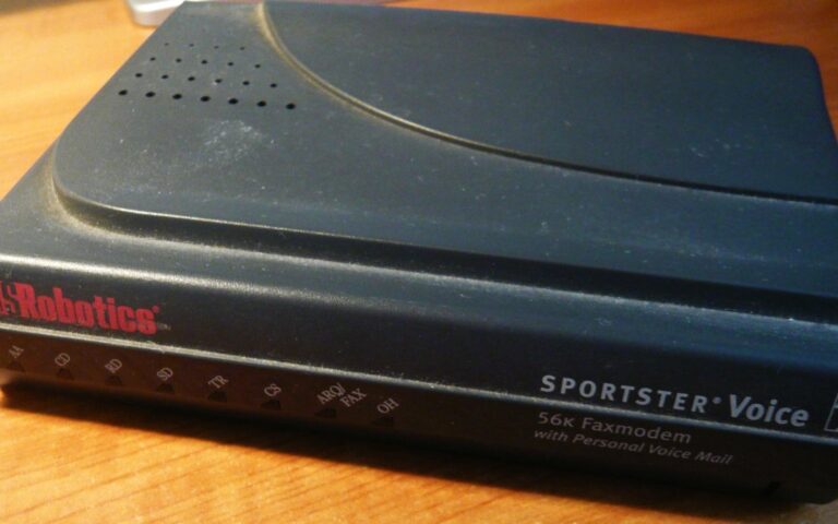 Modem téléphonique US Robotics 56K Sportster Voice, boîtier sombre à voyants, posé sur une table en bois