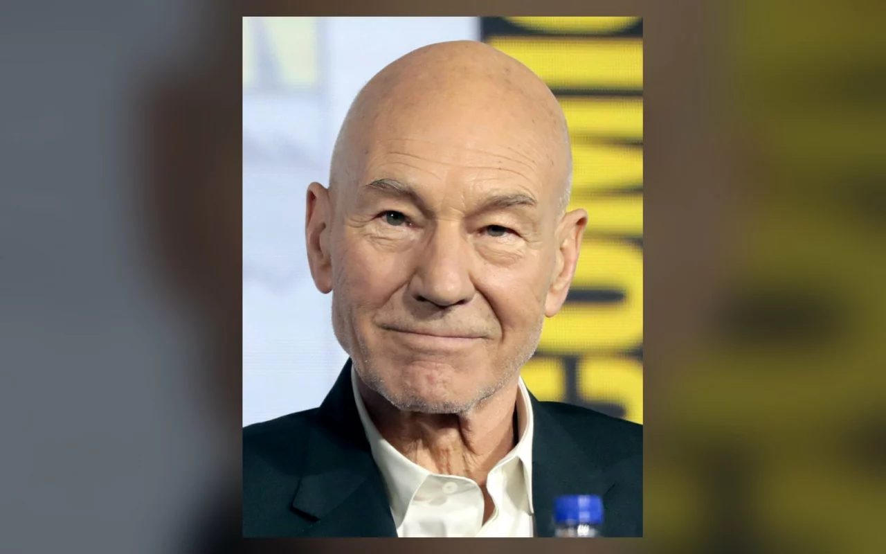 Patrick Stewart, crâne rasé, chemise blanche et veste sombre, sourit sur la scène du Comic-Con de San Diego