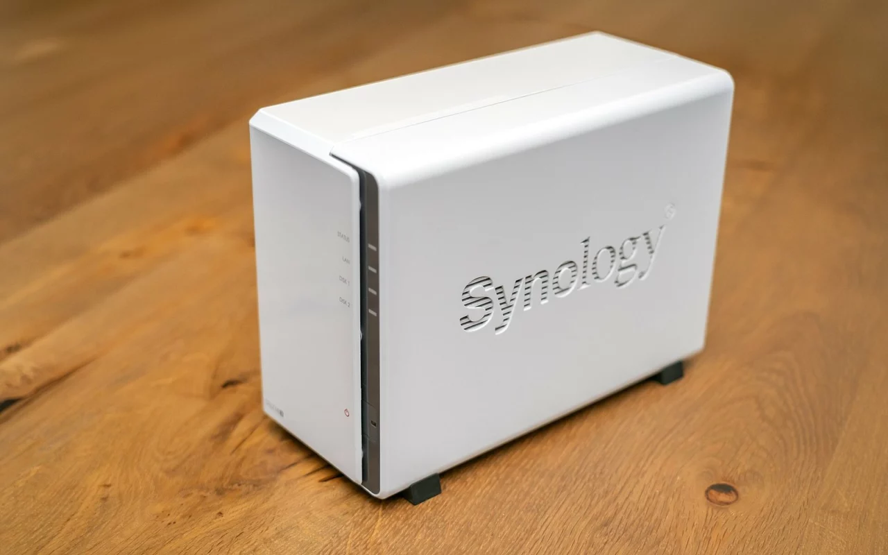 Un petit serveur de stockage Synology DS223j, boîtier blanc à deux disques, posé sur une table en bois