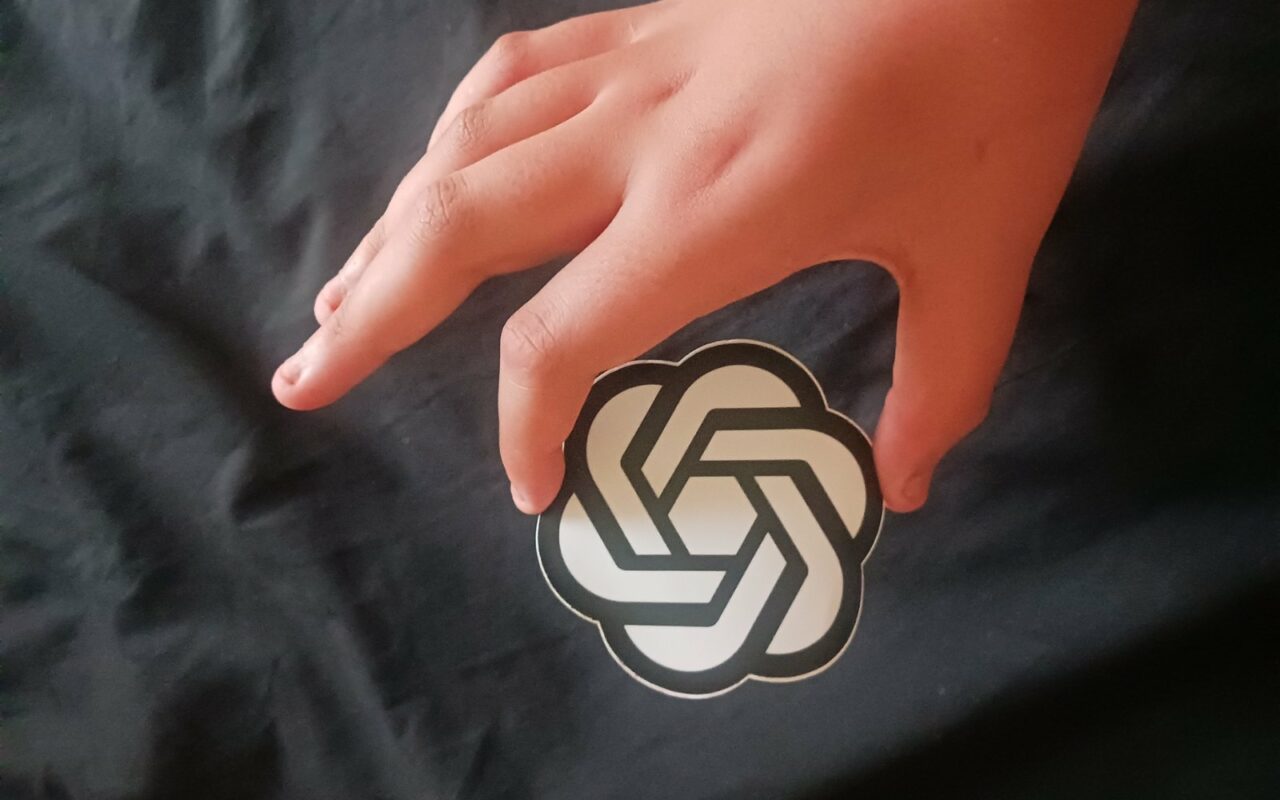 Une main tient un autocollant rond portant le logo d'OpenAI sur un fond de tissu noir