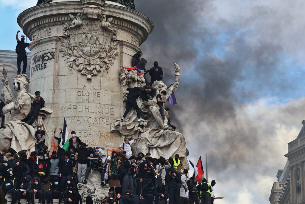 Manifestants vêtus de noir massés au pied et sur le monument de la place de la République, sous une épaisse fumée noire
