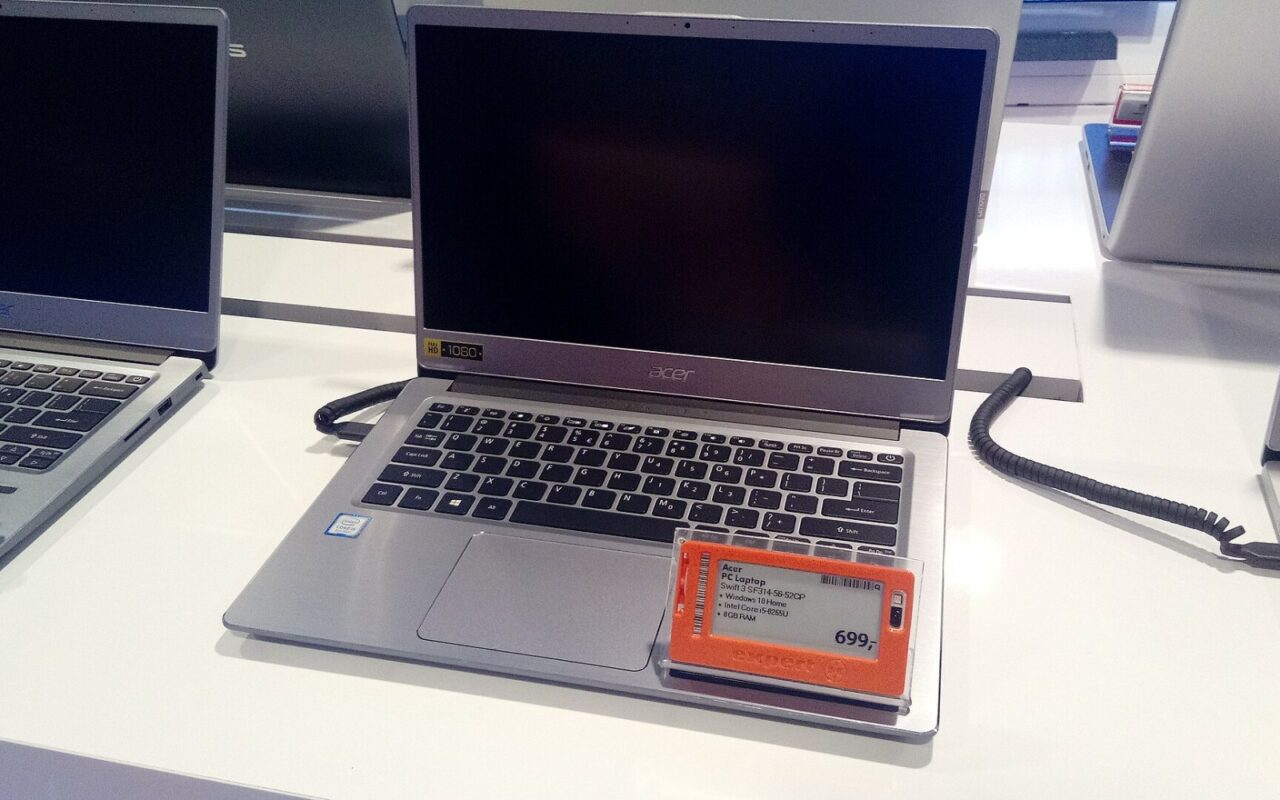 Un ordinateur portable Acer ouvert sur un présentoir de magasin, une étiquette de prix orange posée sur le repose-poignets.