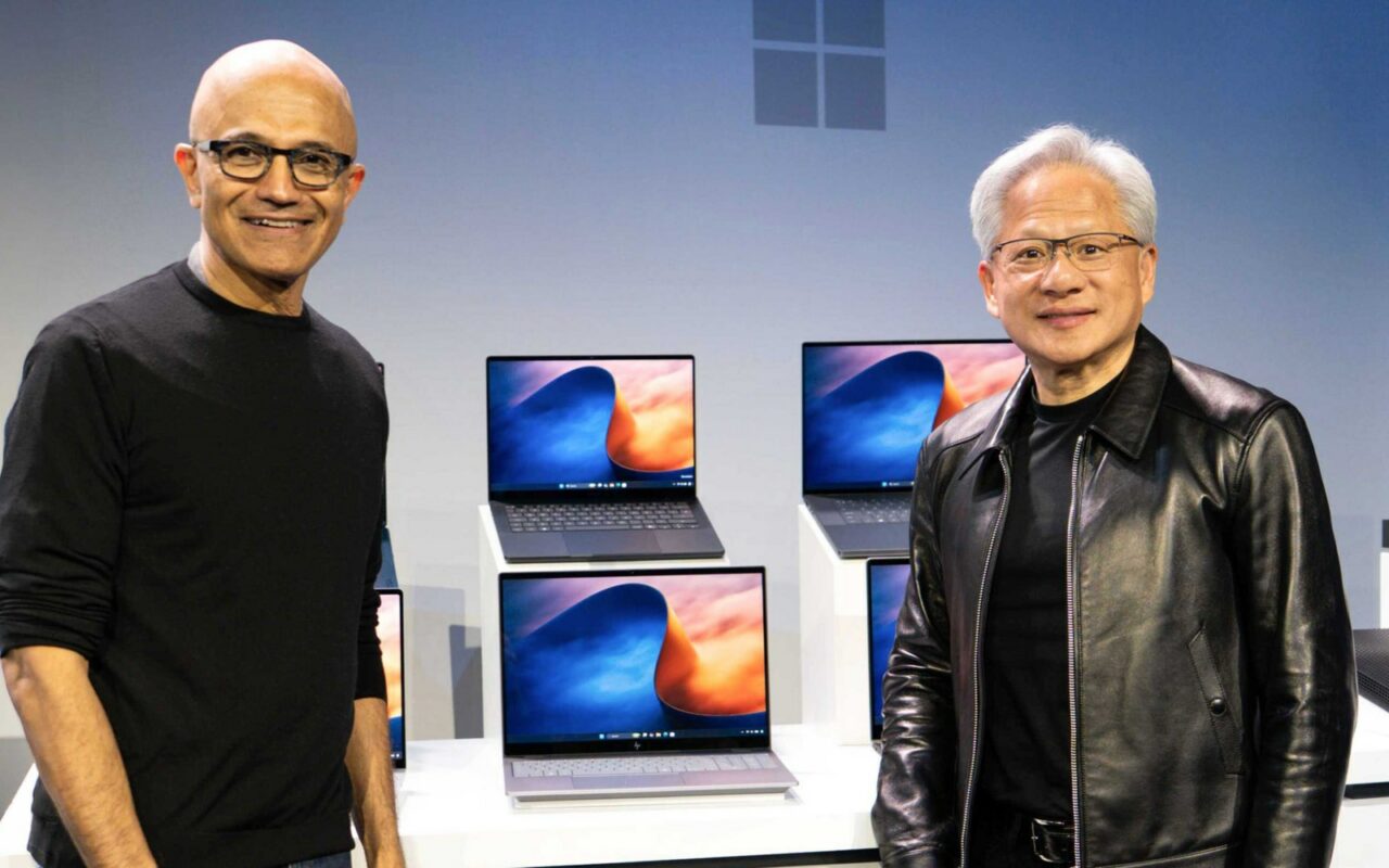 Satya Nadella, patron de Microsoft, et Jensen Huang, patron de Nvidia, posent de part et d'autre d'une table où sont exposés plusieurs portables équipés de la puce RTX Spark.