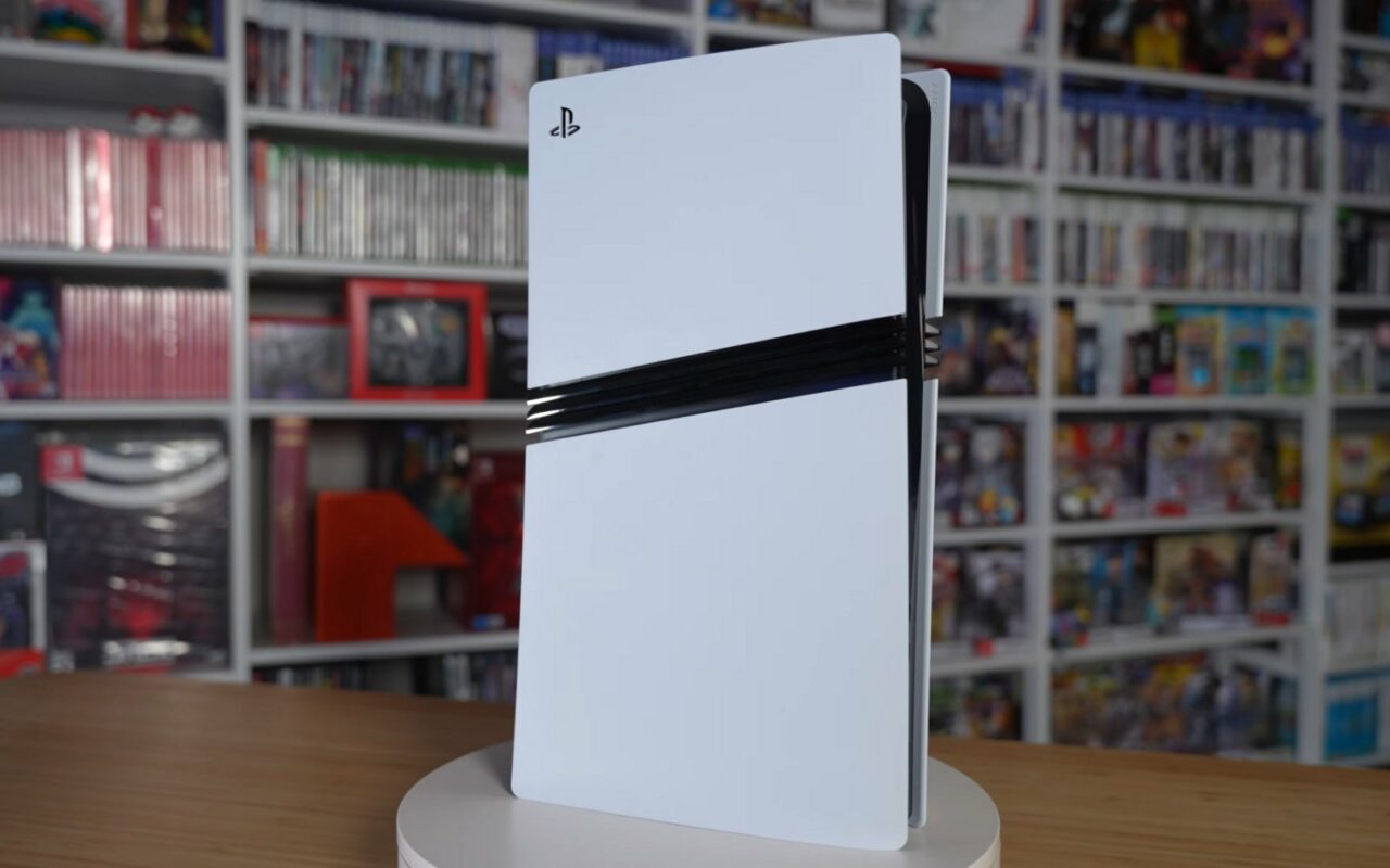 Une console PS5 Pro blanche posée debout sur un socle tournant, devant des étagères remplies de jeux vidéo.