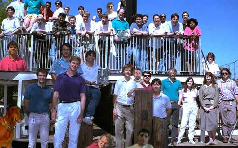 Photo de groupe d'une équipe Apple du début des années 1990, une quarantaine de personnes sur une terrasse en bois, un chien au premier plan