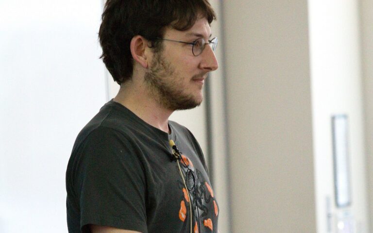 Ryan Dahl, de profil, en tee-shirt sombre, parle devant un écran lors d'une conférence.