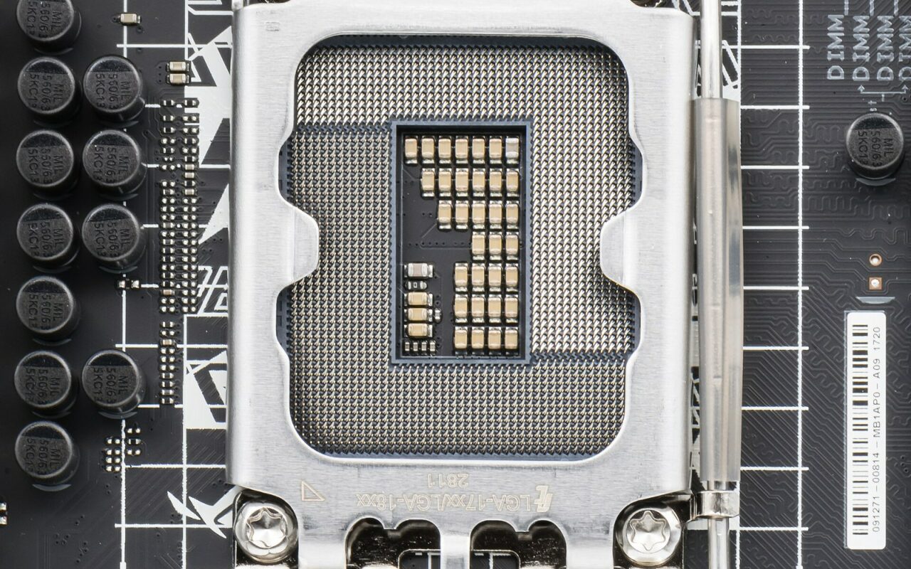 Gros plan sur un socket de processeur LGA1700 vide, avec sa grille de contacts dorés et son levier de verrouillage, sur une carte mère noire.