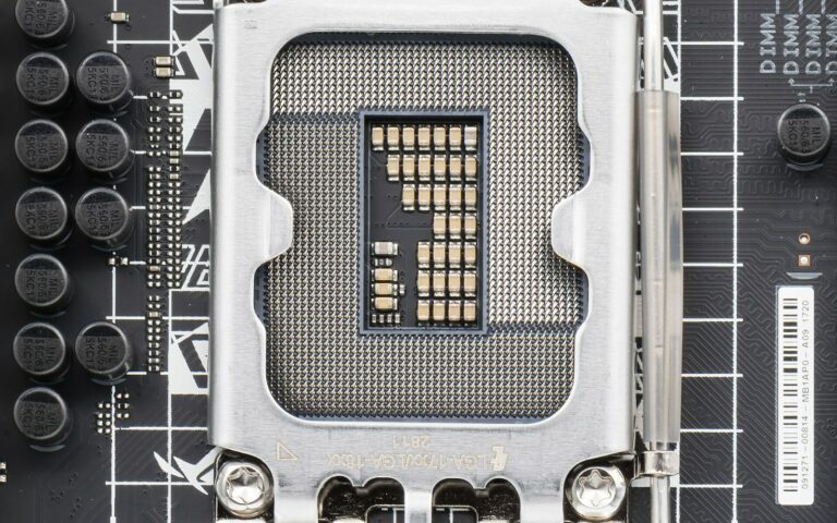 Gros plan sur un socket de processeur LGA1700 vide, avec sa grille de contacts dorés et son levier de verrouillage, sur une carte mère noire.
