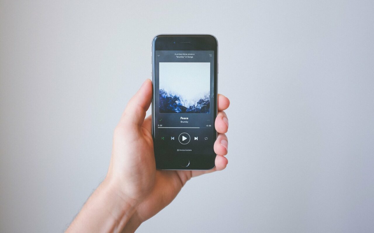 Une main tient un smartphone affichant l'écran de lecture d'un morceau dans Spotify