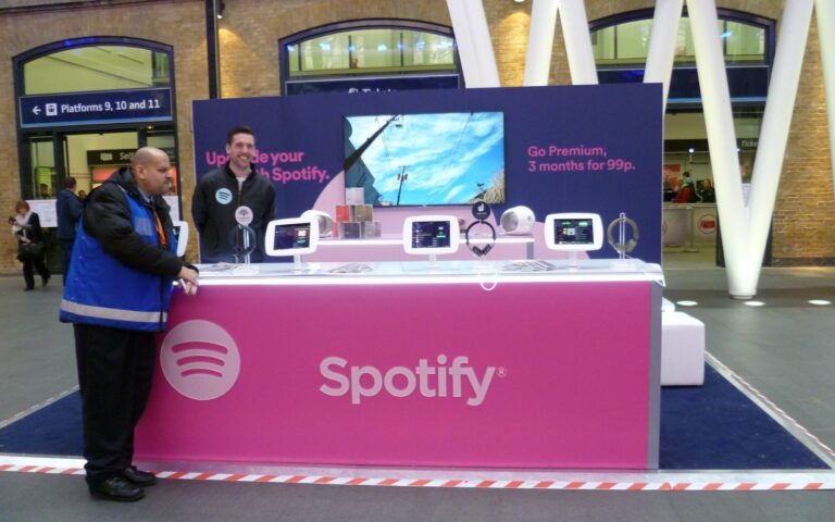 Stand rose de Spotify avec des tablettes, vantant l'abonnement Premium dans une gare.