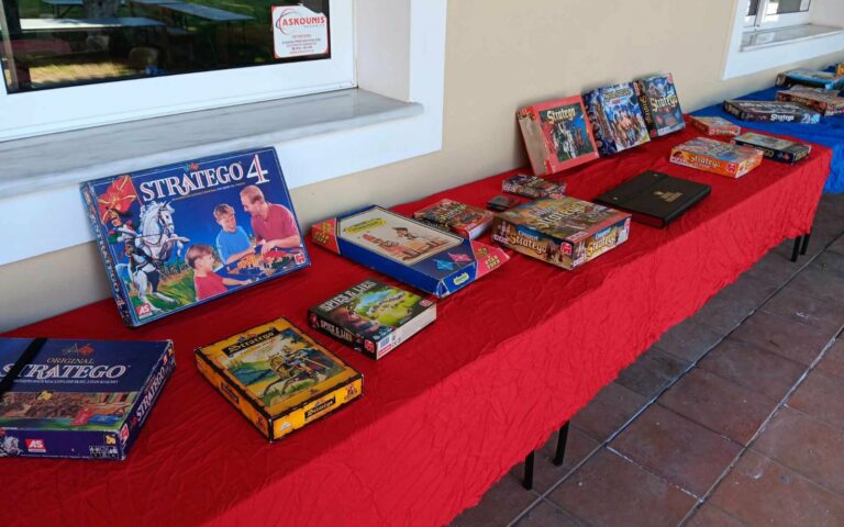Plusieurs boîtes du jeu Stratego de différentes éditions alignées sur une table nappée de rouge lors d'un tournoi.
