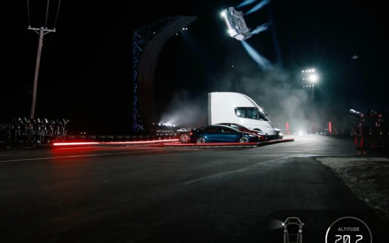 De nuit, une voiture de sport Tesla en l'air au-dessus d'un camion Tesla Semi et de voitures garées, des jets de gaz sous la carrosserie