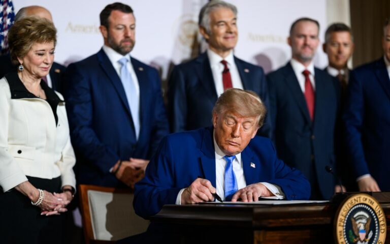 Donald Trump assis à une table signe un décret, entouré de personnes debout, à l'auditorium Andrew W. Mellon de Washington